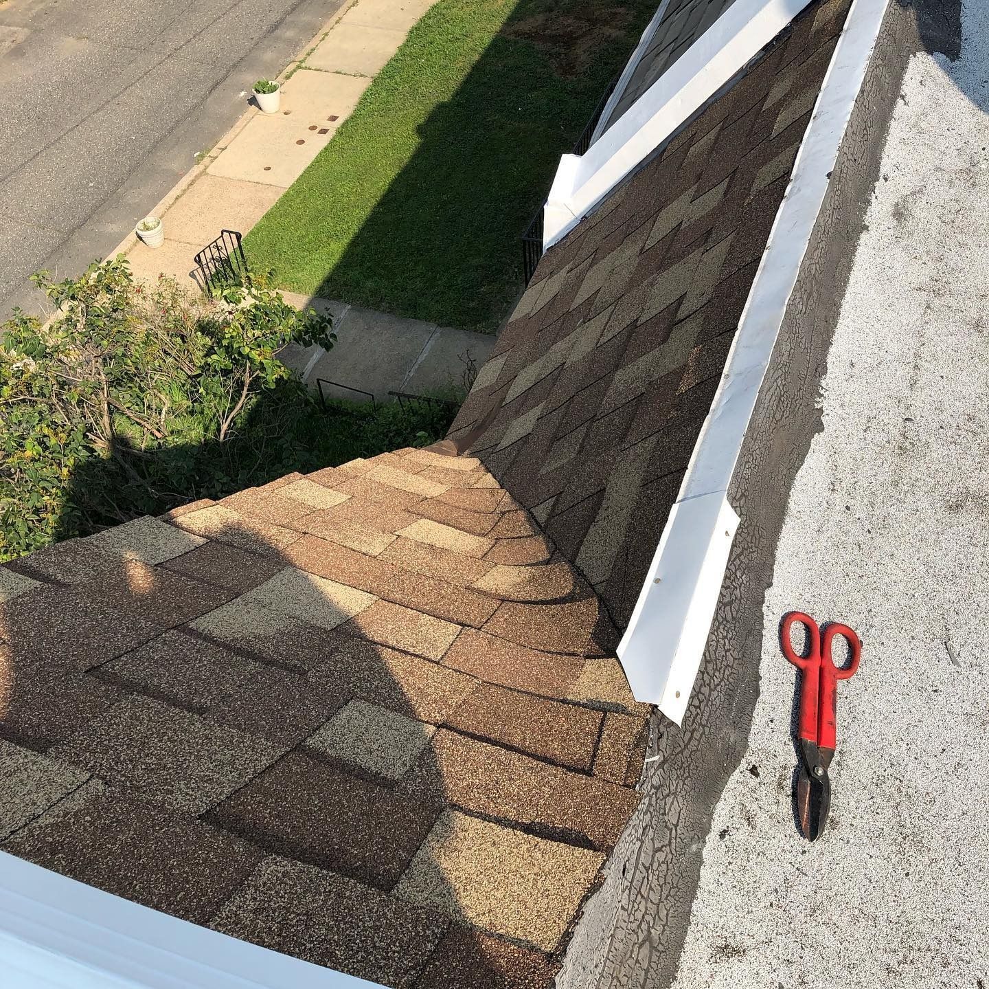 Roof shingles and gutter by a street, with red-handled scissors on the roof edge.