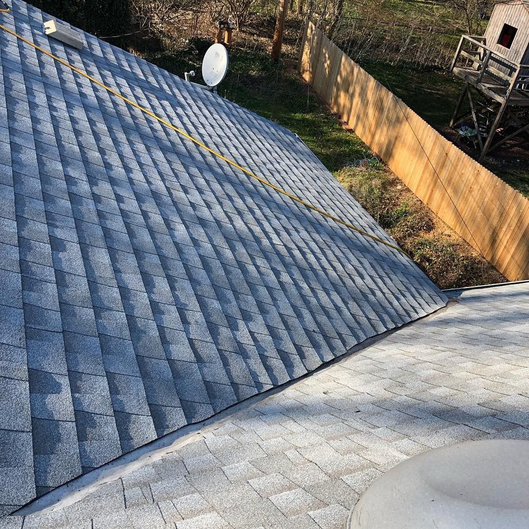 Rooftop with blue shingles, white satellite dish, and concrete edge beside a grassy yard