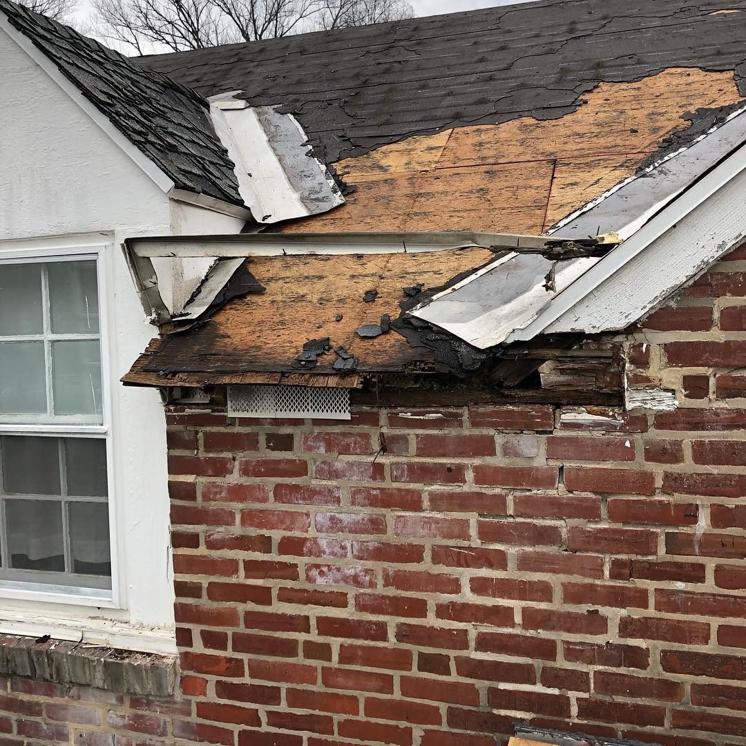 Damaged house roof with missing shingles and exposed wood over a brick wall