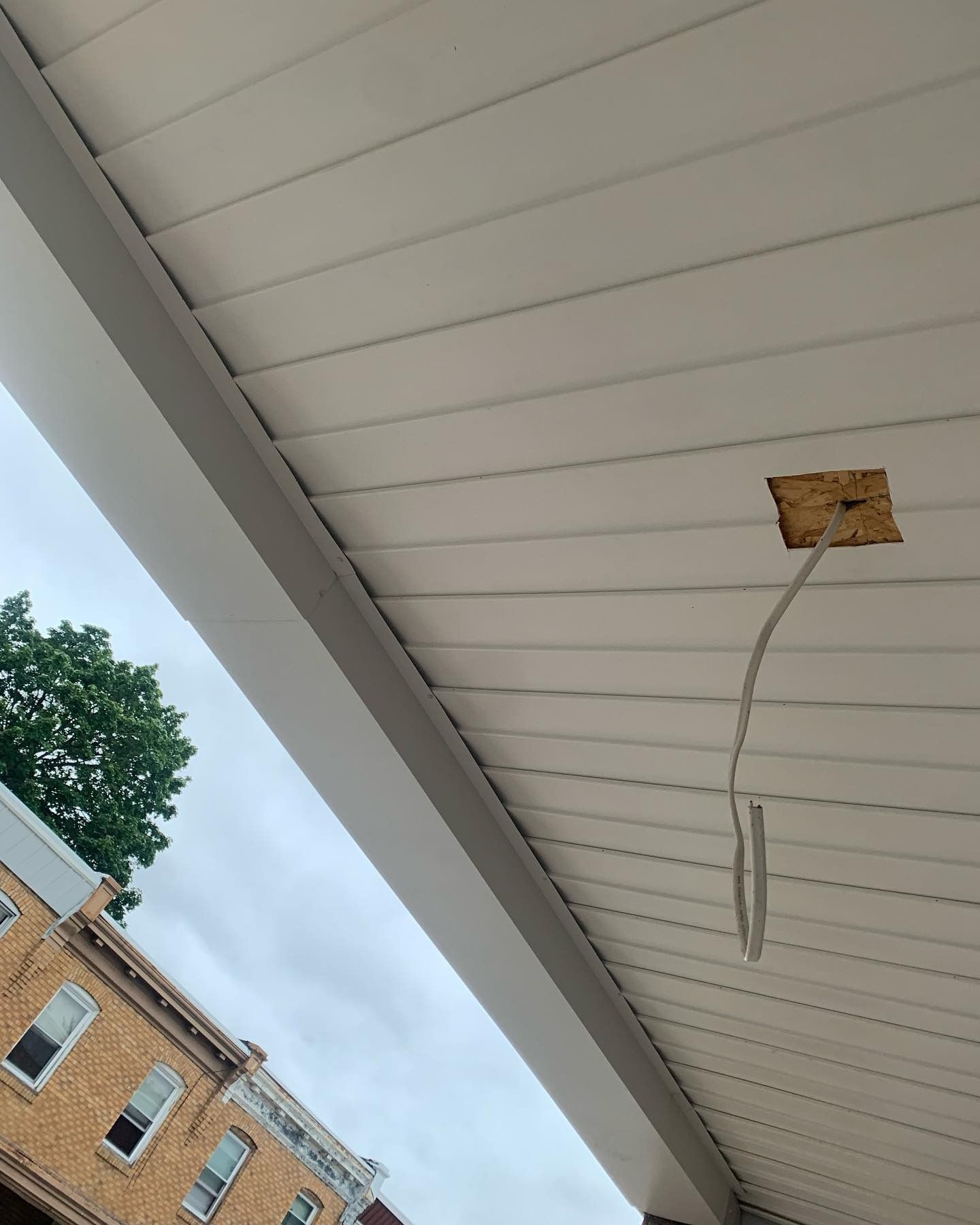 Ceiling under a porch with a dangling electrical wire and a square opening in the paneling