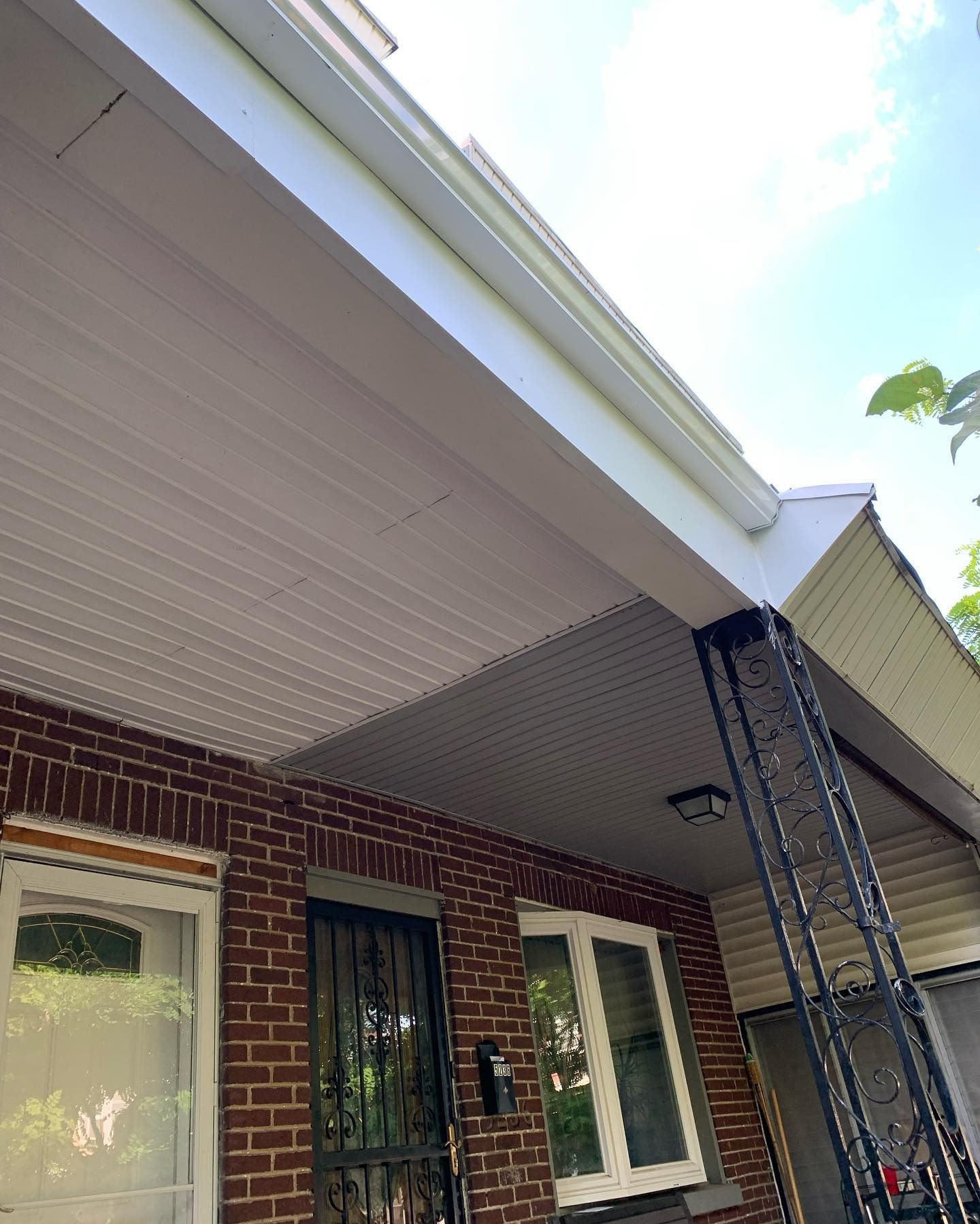 Brick house porch with a white soffit, front door, window, and extension ladders leaning against the roofline