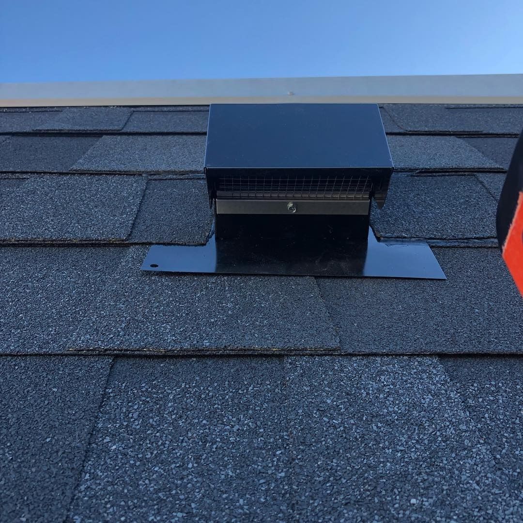 Black roof vent on asphalt shingles under a clear blue sky