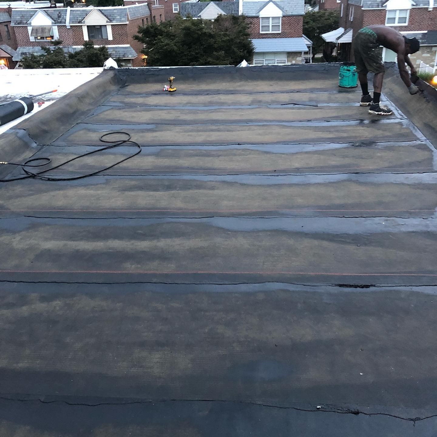 Worker installing roofing on a flat roof with dark tar paper and city houses in the background