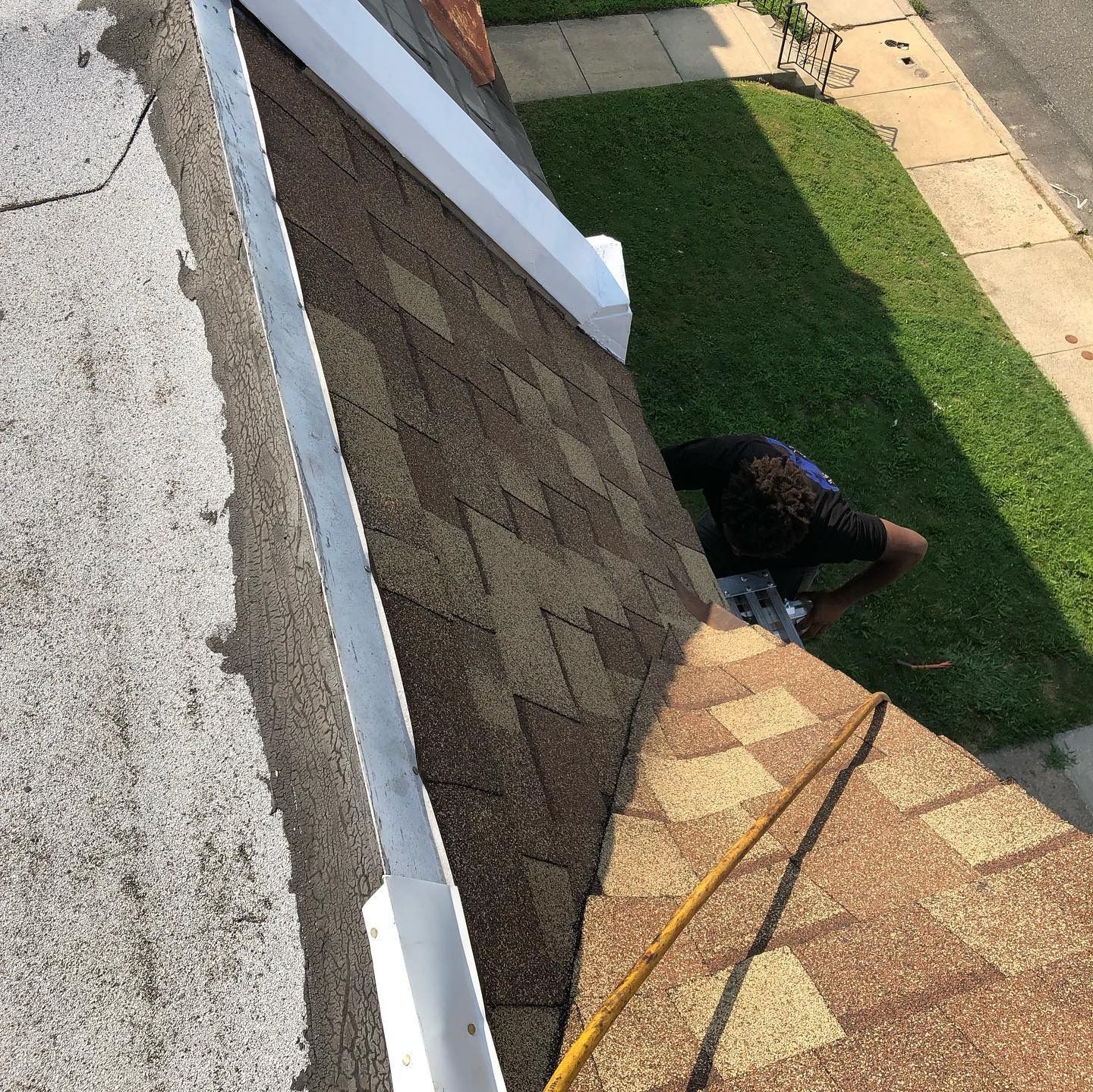 Worker cleaning roof near gutter beside white siding and green lawn