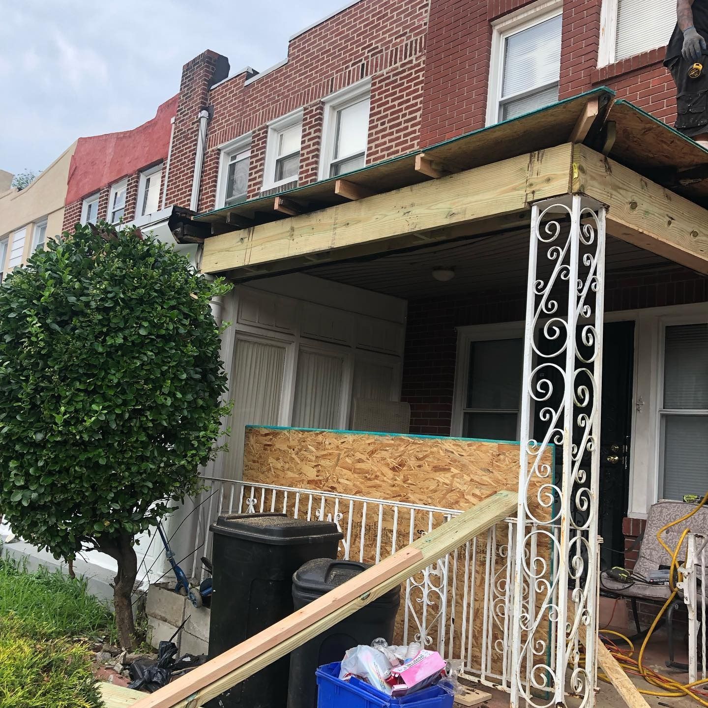 Brick row house with a covered porch, white wrought-iron railing, and boarded front entry.