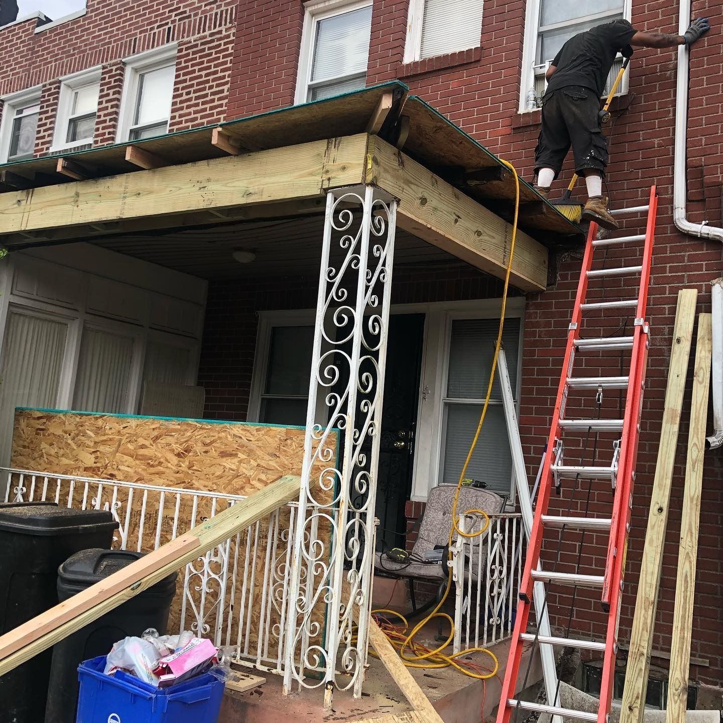 Worker on ladder repairing the roof of a brick row house with exposed decking and white metal railing