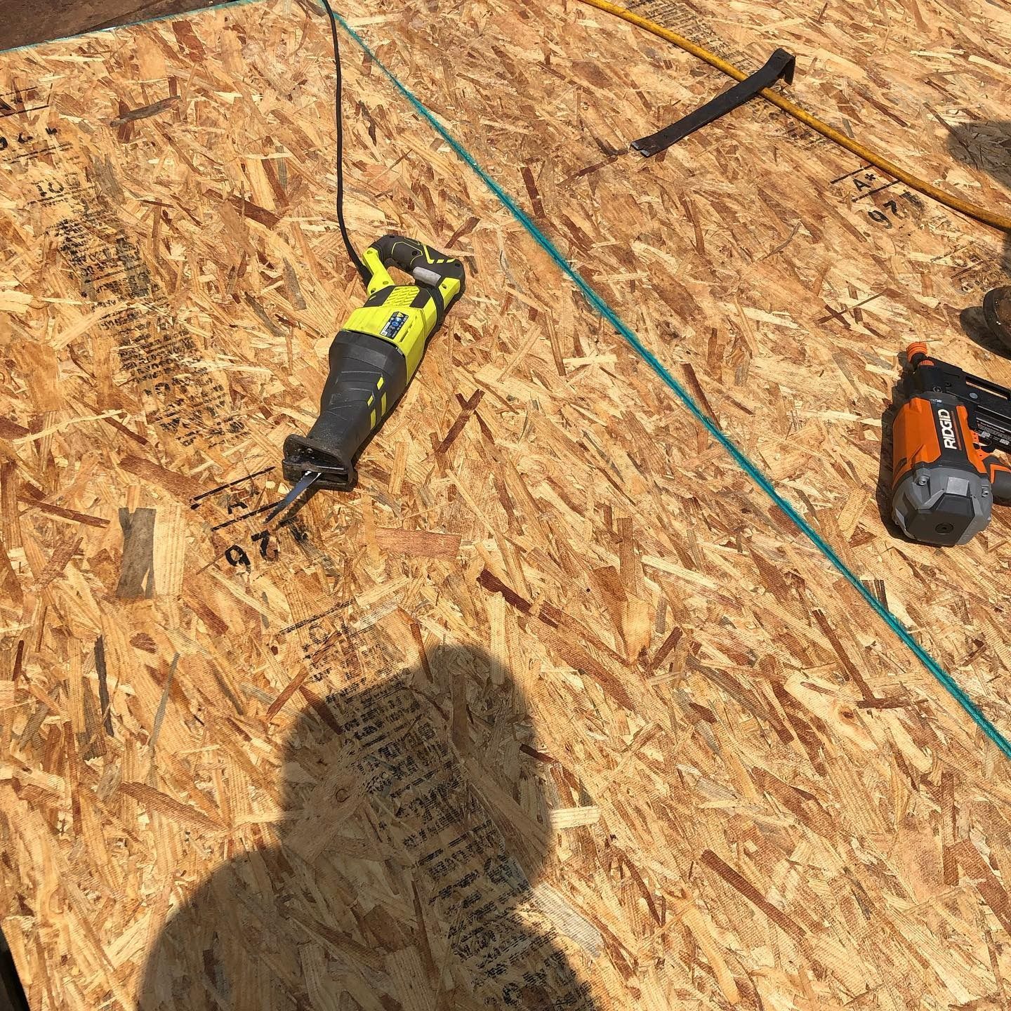 Two power drills and a hammer on plywood roof decking with a blue chalk line.