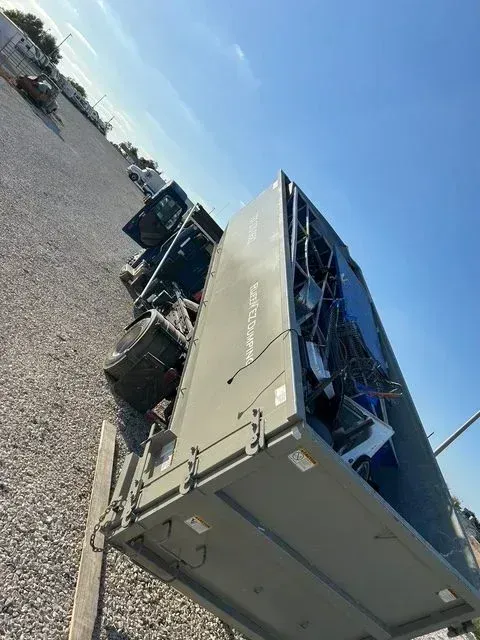 A large, gray industrial dumpster filled with scrap metal sits on a gravel lot under a clear blue sky. Dumpster rental Pflugerville TX