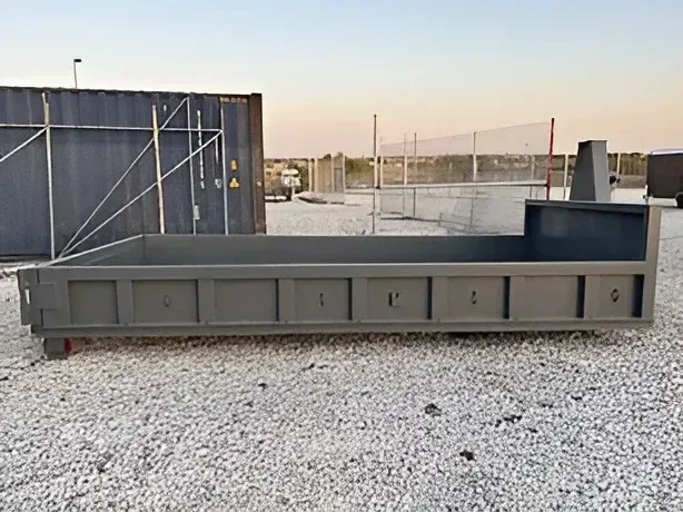 A grey metal industrial roll-off dumpster sits on a gravel surface outdoors. 6 yard dumpster Pflugerville TX