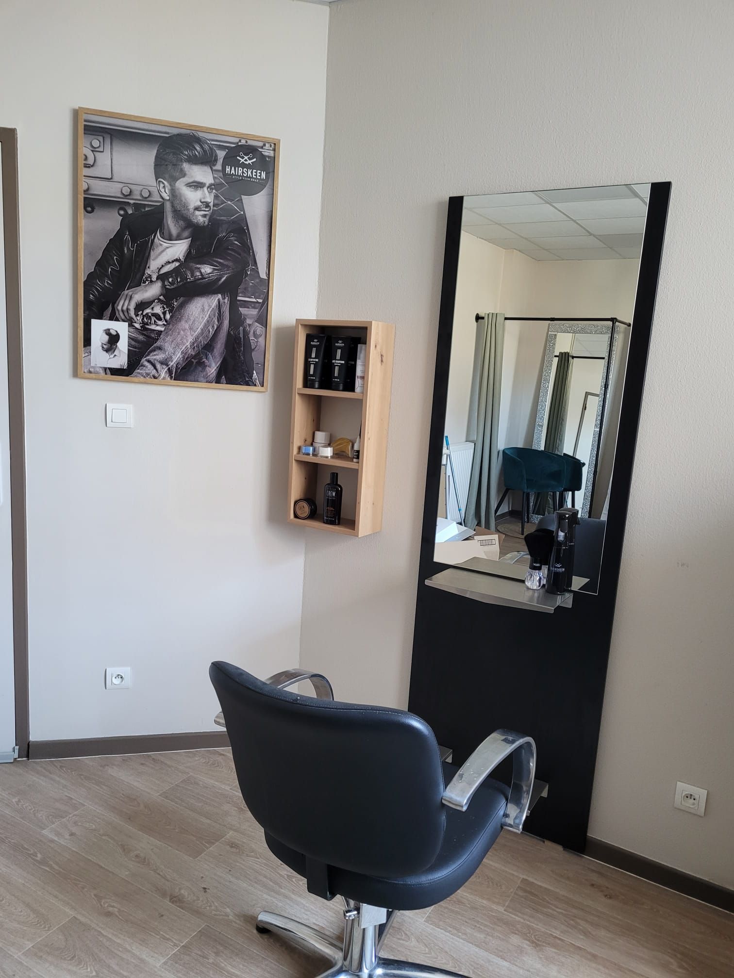 Un salon de coiffure avec une chaise, un miroir et un tableau au mur.