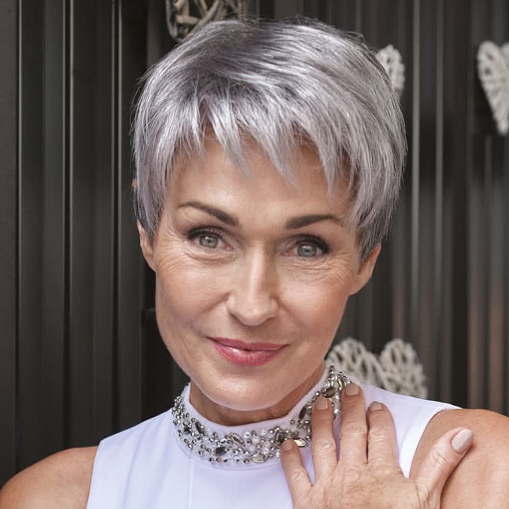 Une femme aux cheveux gris courts porte une robe blanche et un collier.