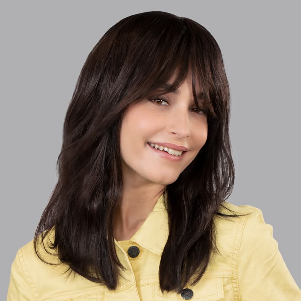 Une femme portant une perruque et une veste jaune sourit.