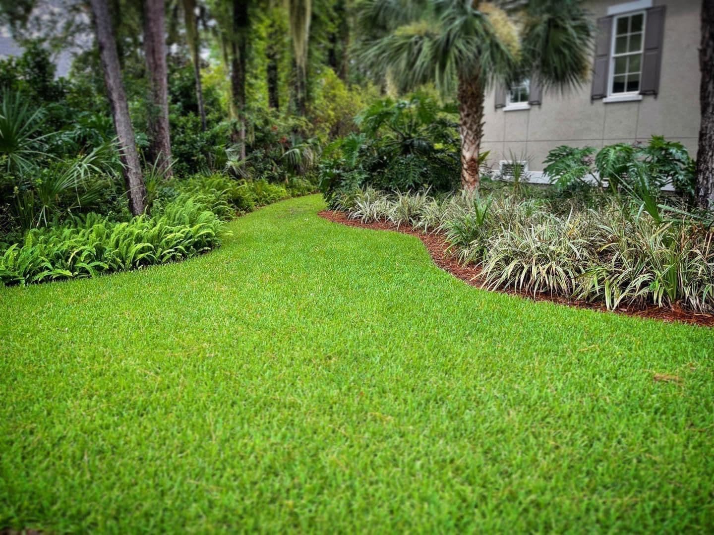 A lush green lawn in front of a house surrounded by trees and bushes.