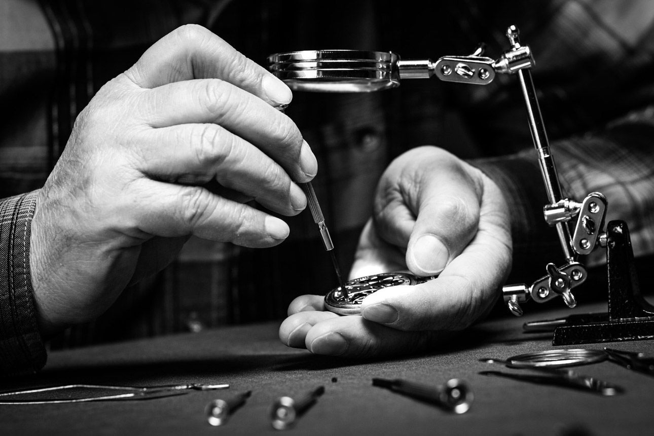 A man is working on a watch with a magnifying glass A man is working on a watch with a magnifying glass