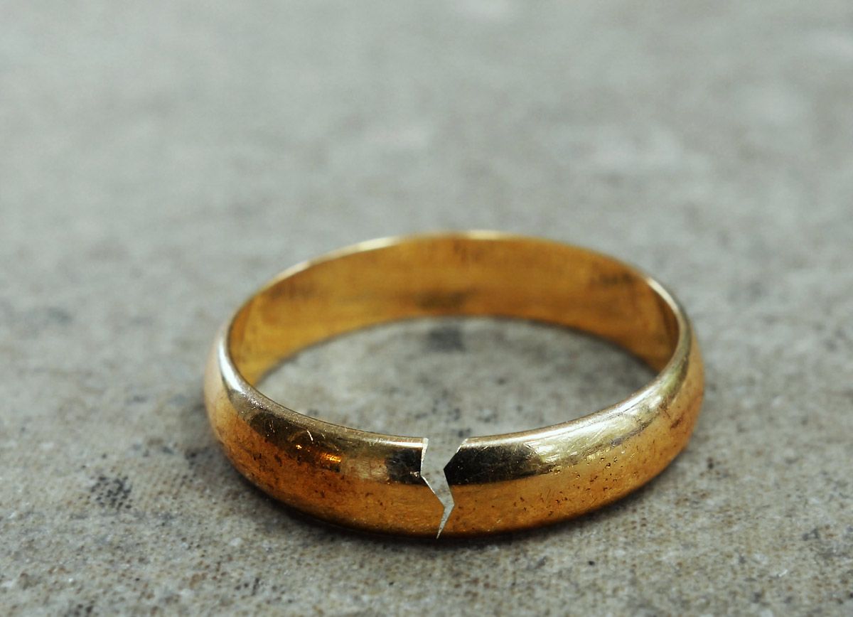 A broken gold wedding ring is sitting on a concrete surface A broken gold wedding ring is sitting on a concrete surface