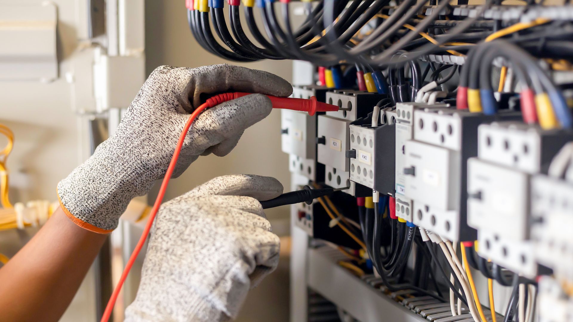 An electrician is working on an electrical box with a multimeter.