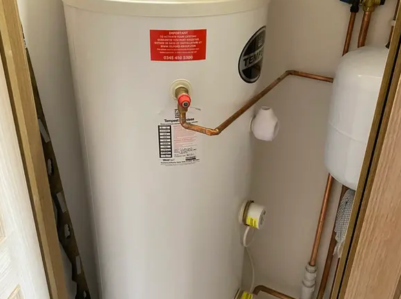 A white water heater is sitting in a corner of a room next to copper pipes.