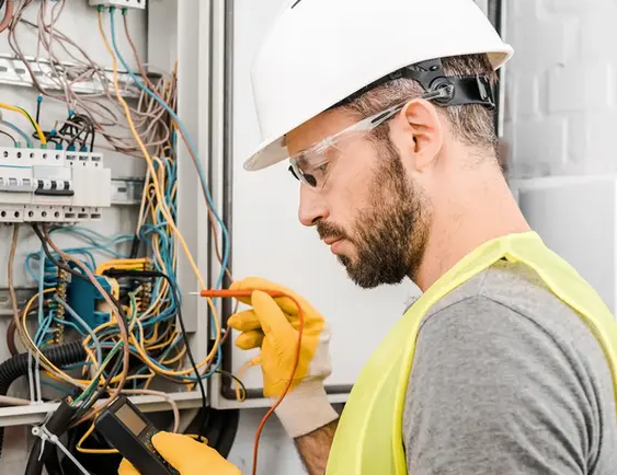 A man wearing a hard hat and safety vest is working on an electrical box.