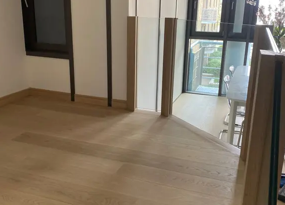 A room with a wooden floor and stairs leading up to a balcony.