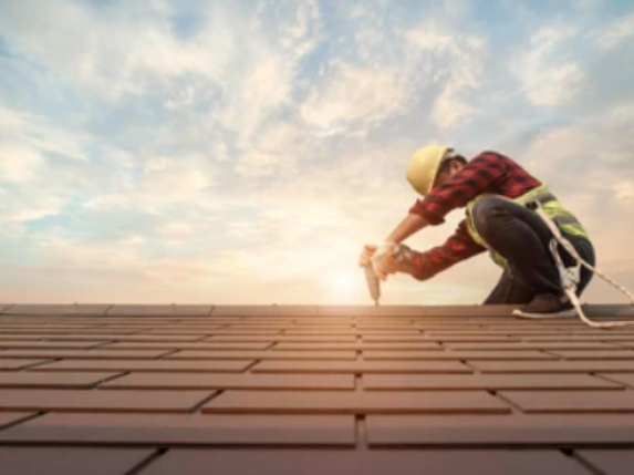 A construction worker is working on a roof with a hammer.