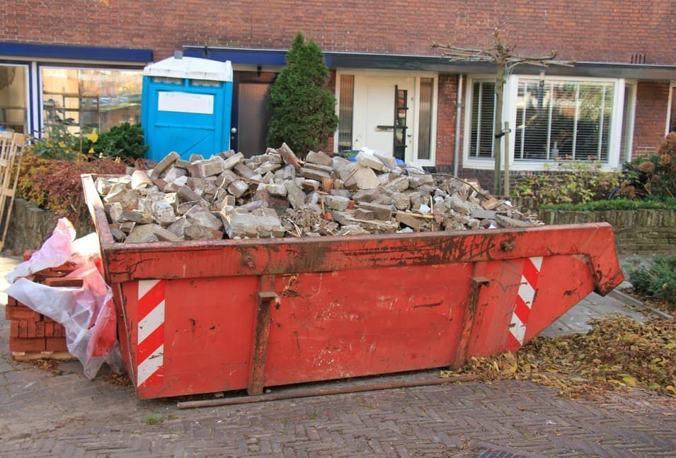 A Red Dumpster Filled With Bricks is in Front of a Brick House — Totally Skip Bins in Yarrabilba, QLD