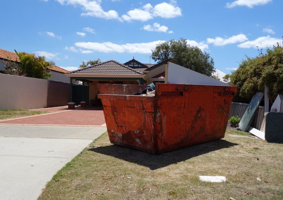 A Large Orange Dumpster is Sitting in Front of a House — Totally Skip Bins in Cryna, QLD