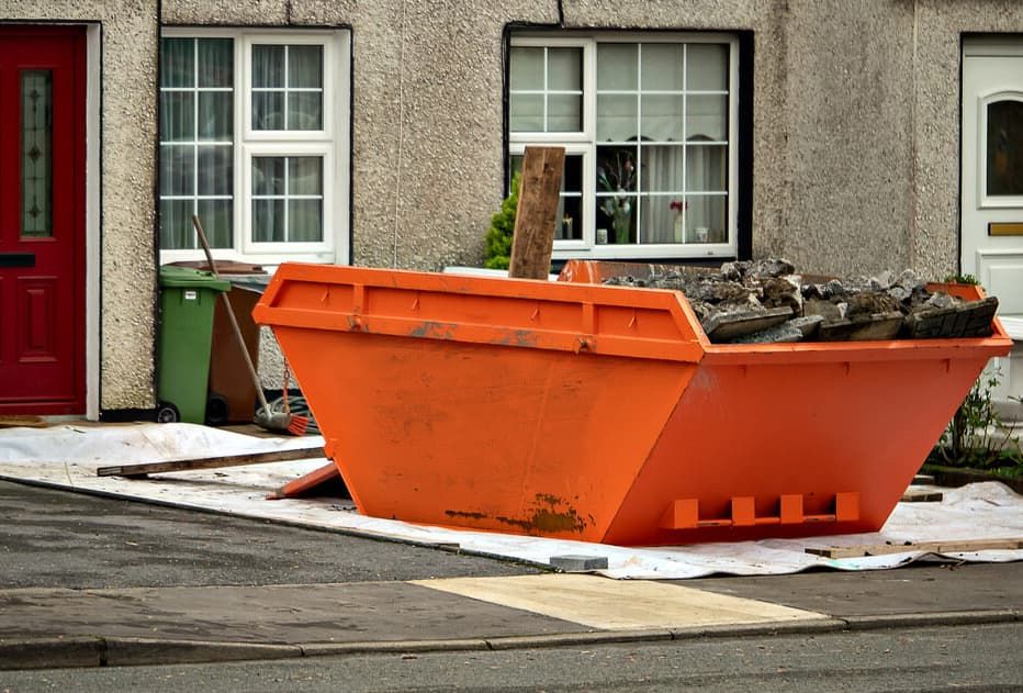 A Large Orange Dumpster is Sitting in Front of a House — Totally Skip Bins in Flagstone, QLD