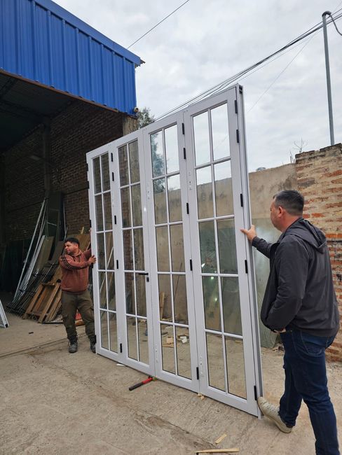 Dos trabajadores sostienen un gran marco de puerta de metal blanco en el exterior de un edificio en construcción.