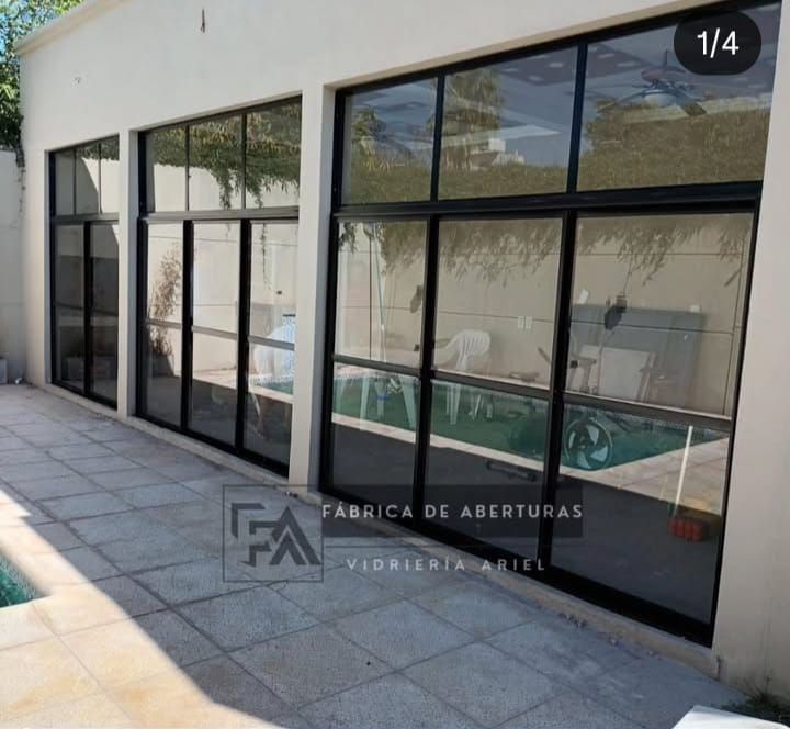 Puertas y ventanas corredizas de vidrio con marcos negros a lo largo de un patio moderno con piso de baldosas.