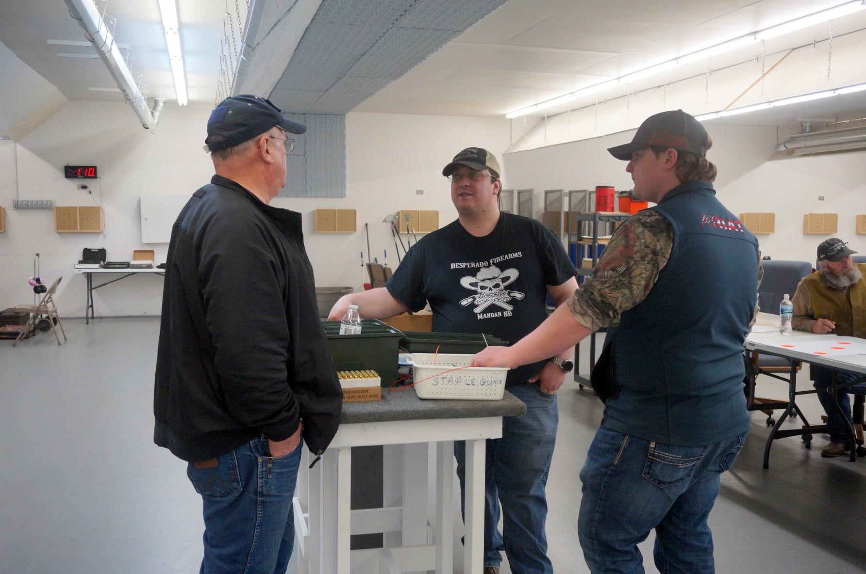 Three men are standing around a table in a room talking to each other.