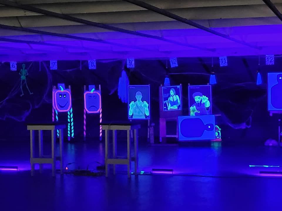 Indoor shooting range with targets lit by blue light; some shaped like figures and faces.