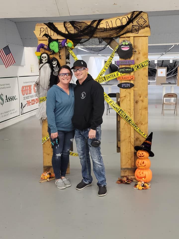 A man and a woman are posing for a picture in front of a wooden arch decorated for halloween.