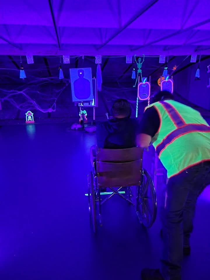 A man in a glow in the dark vest is pushing a man in a wheelchair.