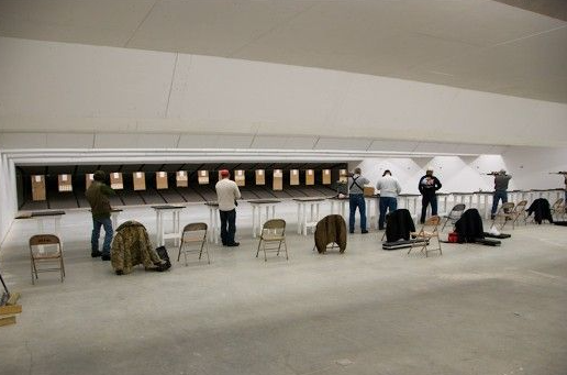 People shooting guns at targets in a white indoor shooting range.