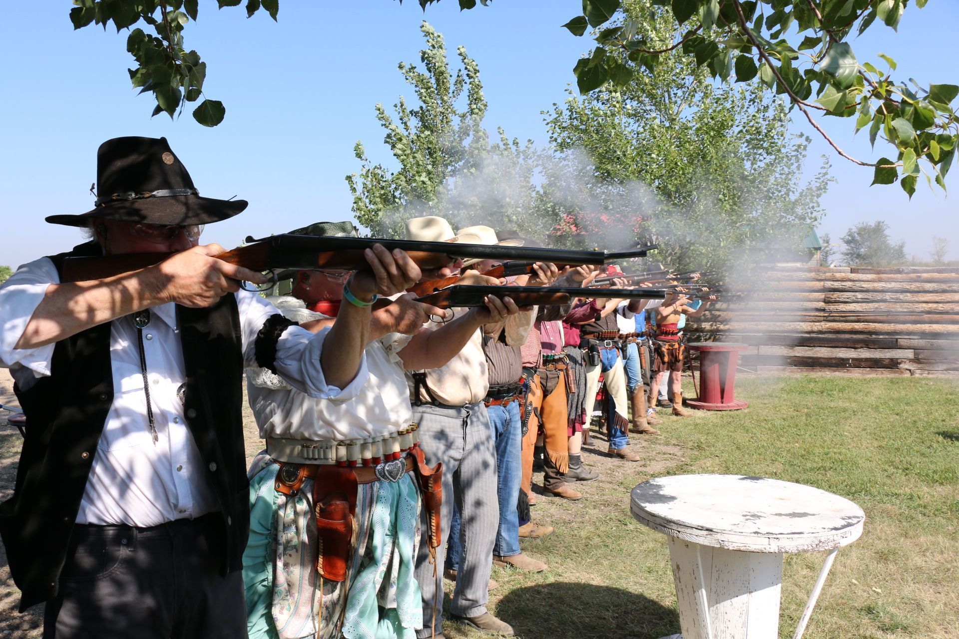 Cowboys firing rifles in a line outdoors, smoke visible.