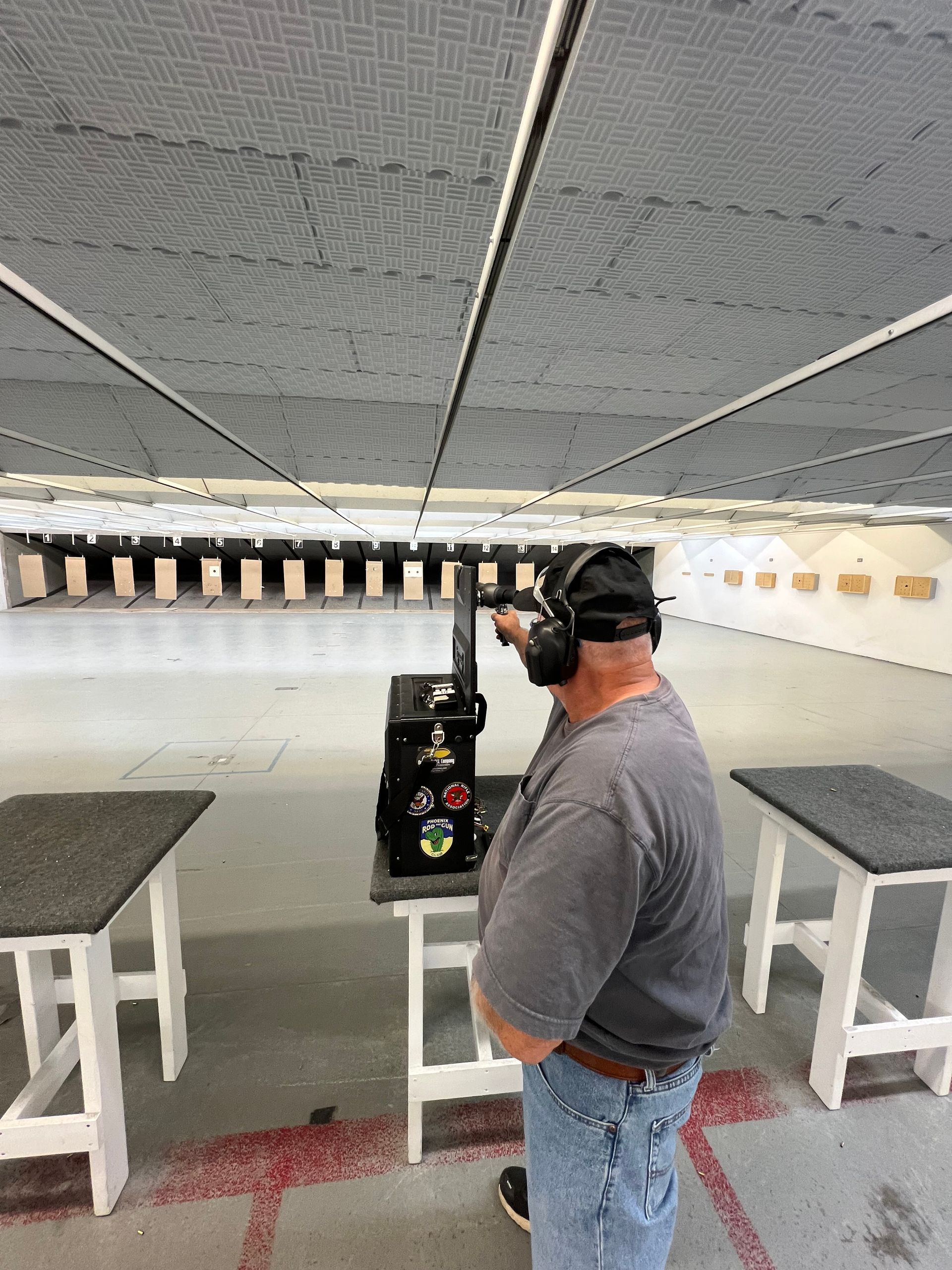 Man in a shooting range, aiming a gun at a target. He wears hearing protection.