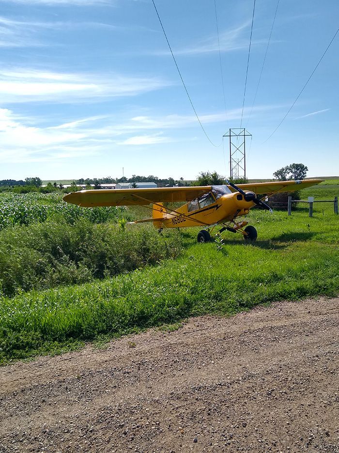 A small yellow plane is parked on the side of a dirt road in a field.