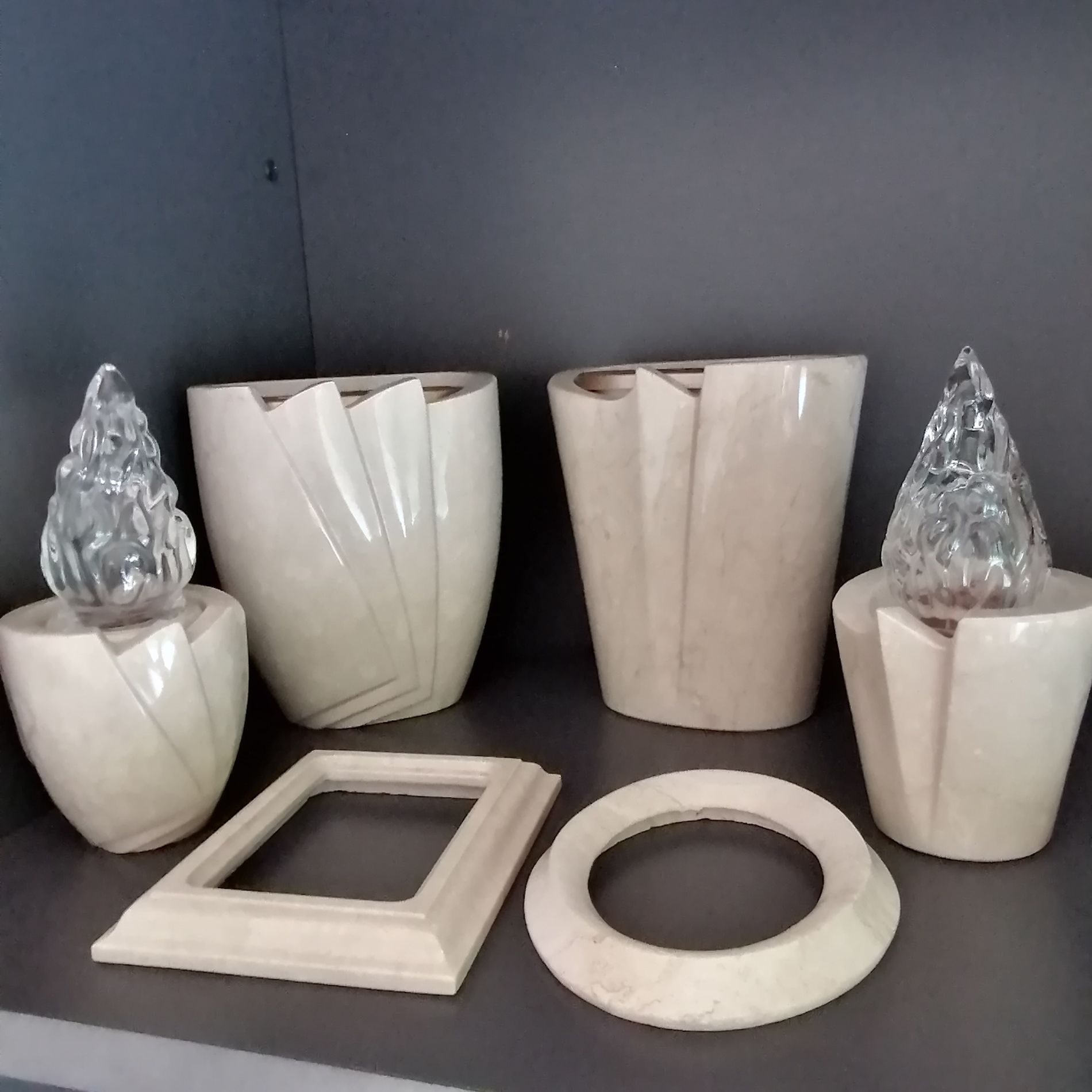 Vari vasi e portacandele in ceramica beige con dettagli in vetro trasparente su una mensola scura.