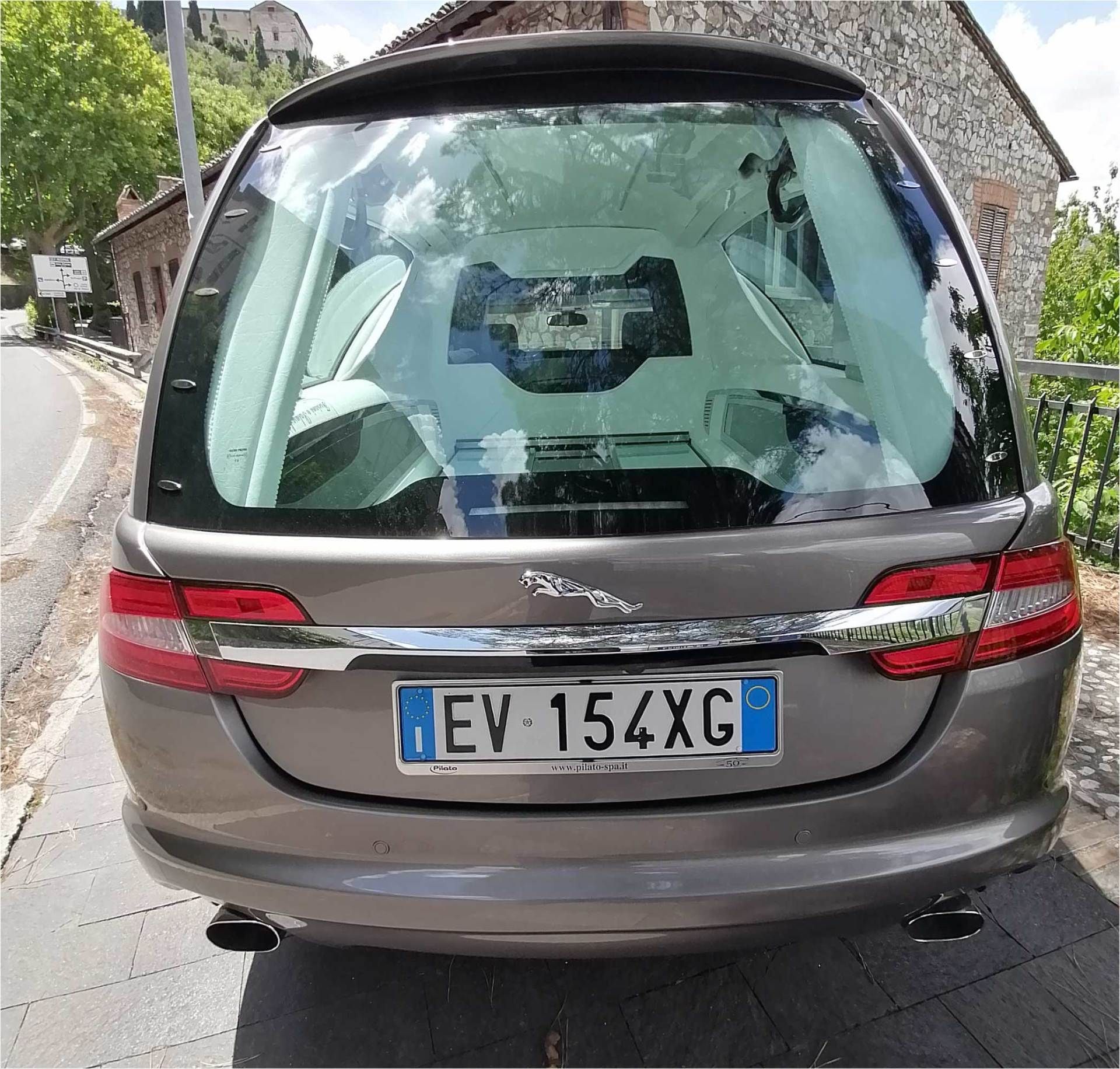 Vista posteriore di un'auto hatchback grigia parcheggiata in una strada stretta, con targa ben visibile.