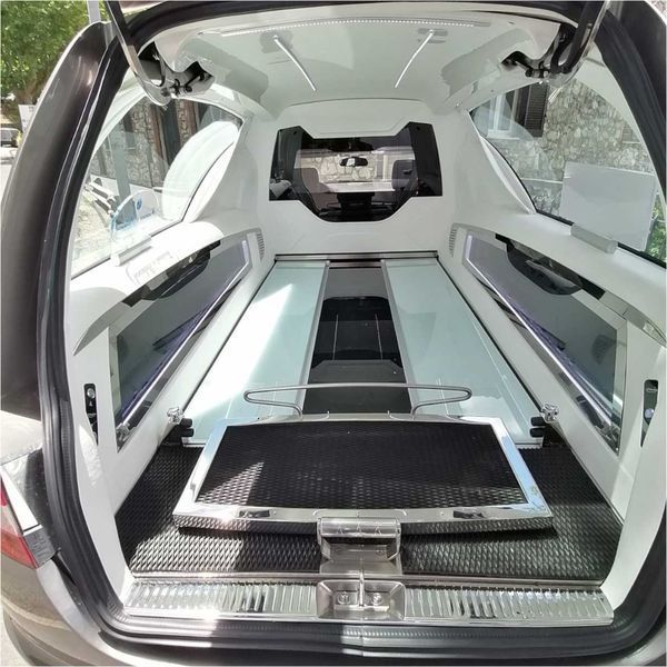 Vista posteriore dell'interno di un carro funebre con piattaforma per la bara e finiture bianche e nere.