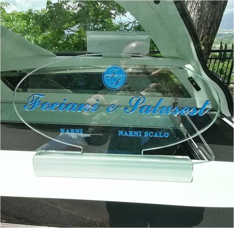 Targa di riconoscimento in vetro con scritta blu in corsivo su un cruscotto bianco di un'auto.