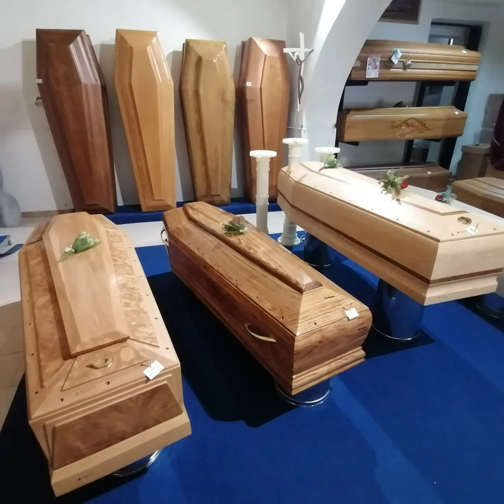 Bare di legno esposte in una sala espositiva di un'impresa di pompe funebri, su un tappeto blu.