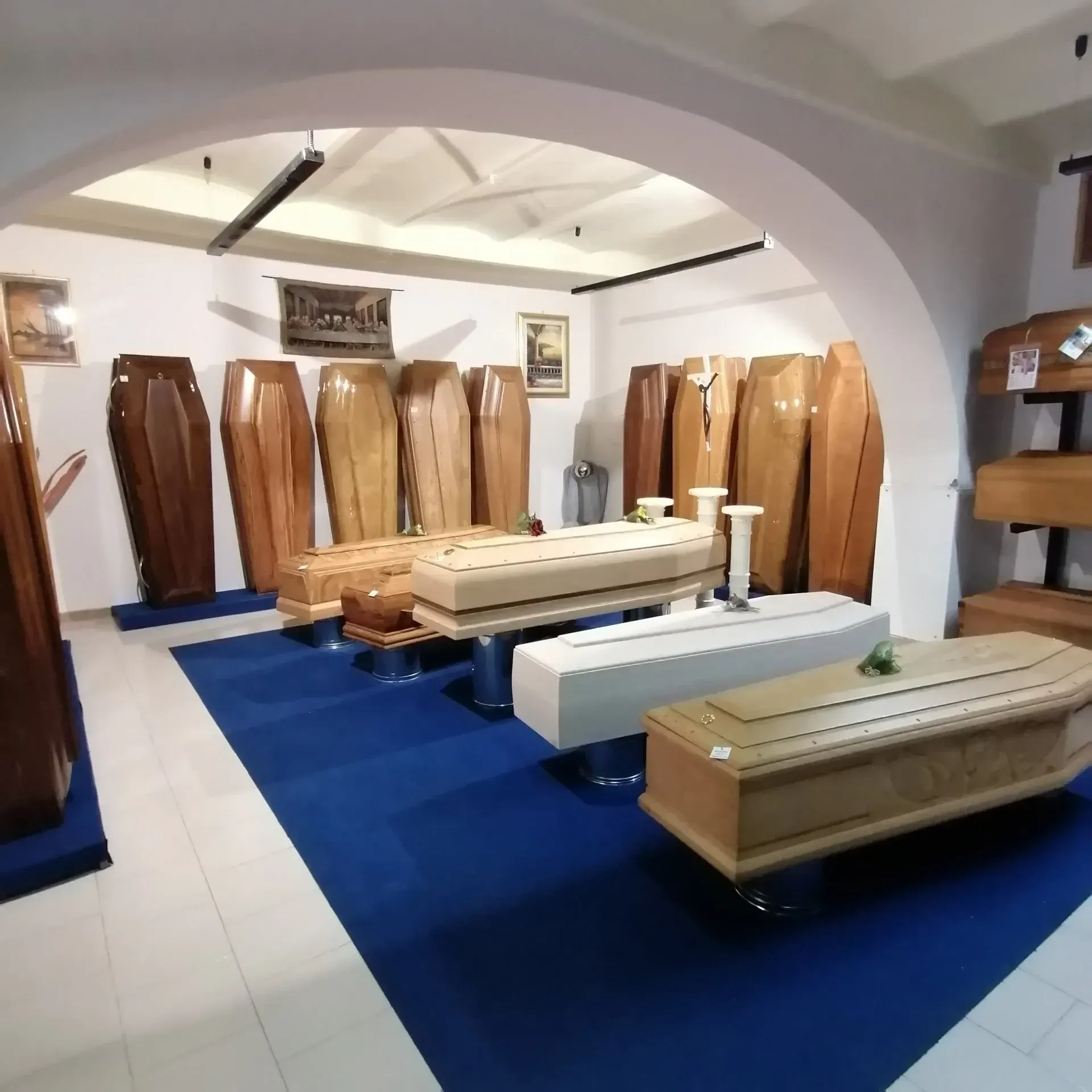 Showroom di mobili con bare e casse funebri in legno esposte su un tappeto blu