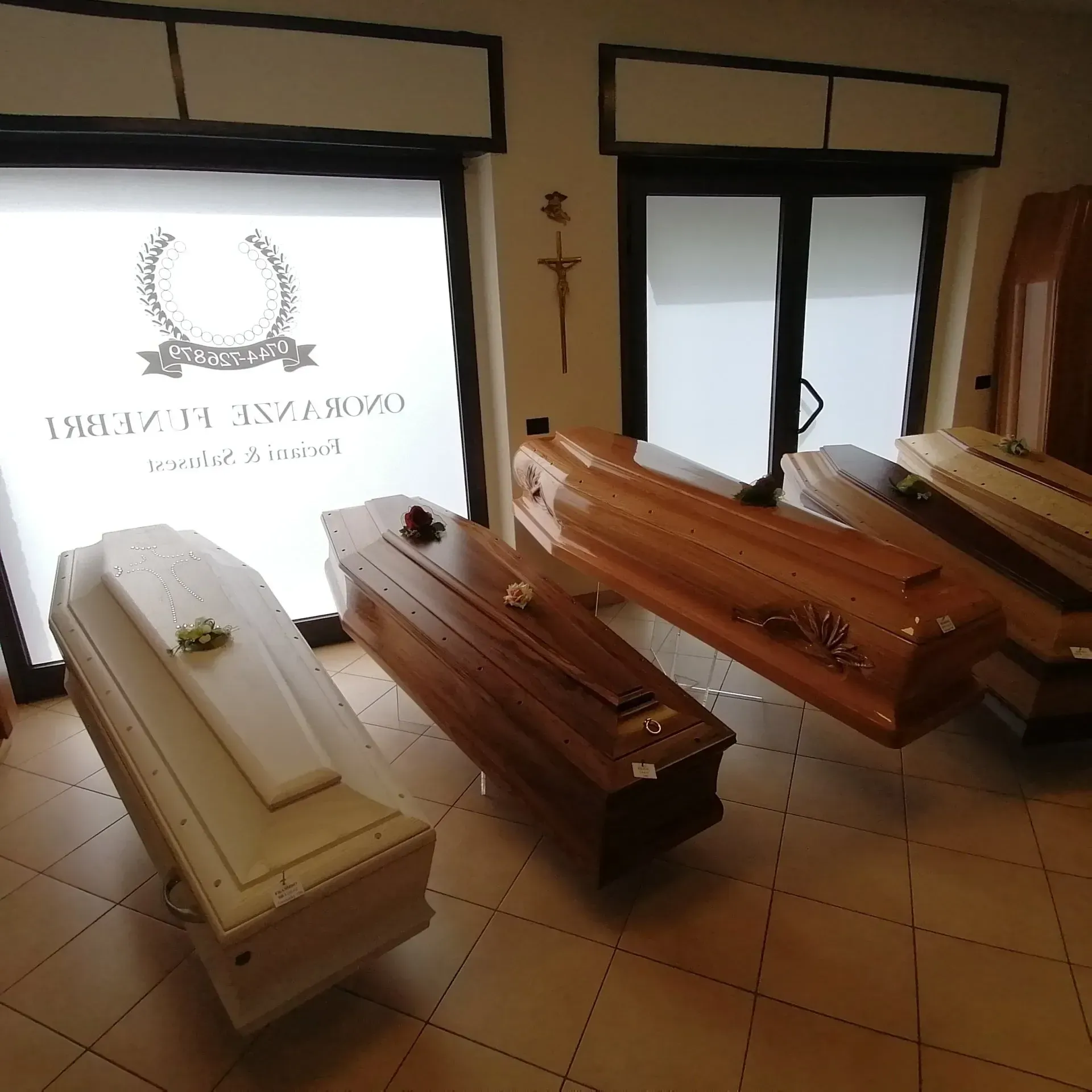Una fila di bare decorate nella sala di veglia funebre di un'agenzia di pompe funebri, con finestre e pavimento piastrellato.