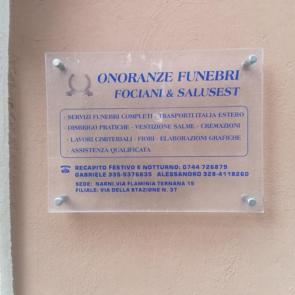 Targa per ONORANZE FUNEBRI FIOCANI & SALIS, testo blu su pannello in acrilico trasparente montato a parete.