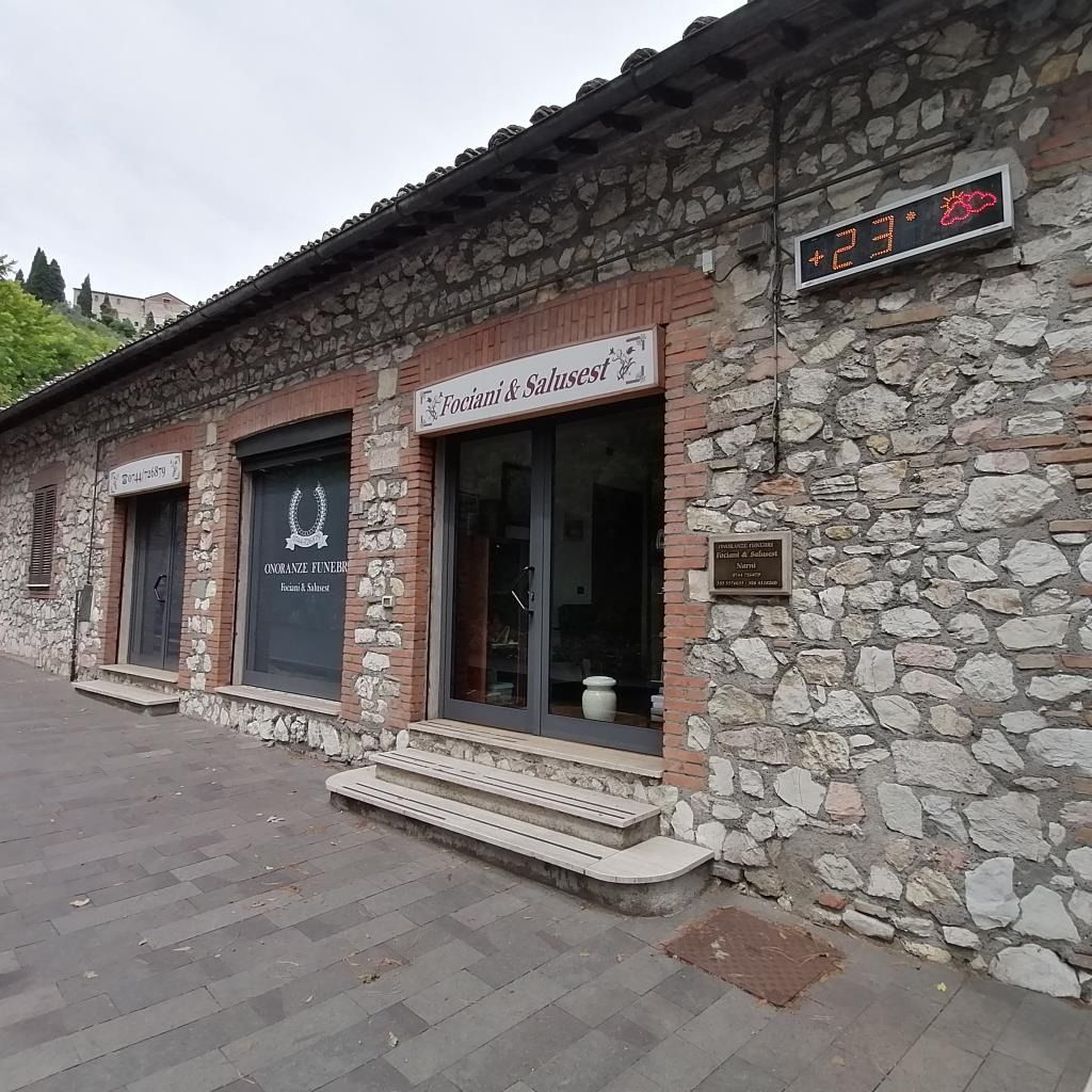 Negozio con facciata in pietra, porta nera, ingresso in vetro e insegna a LED rossa su una strada asfaltata.