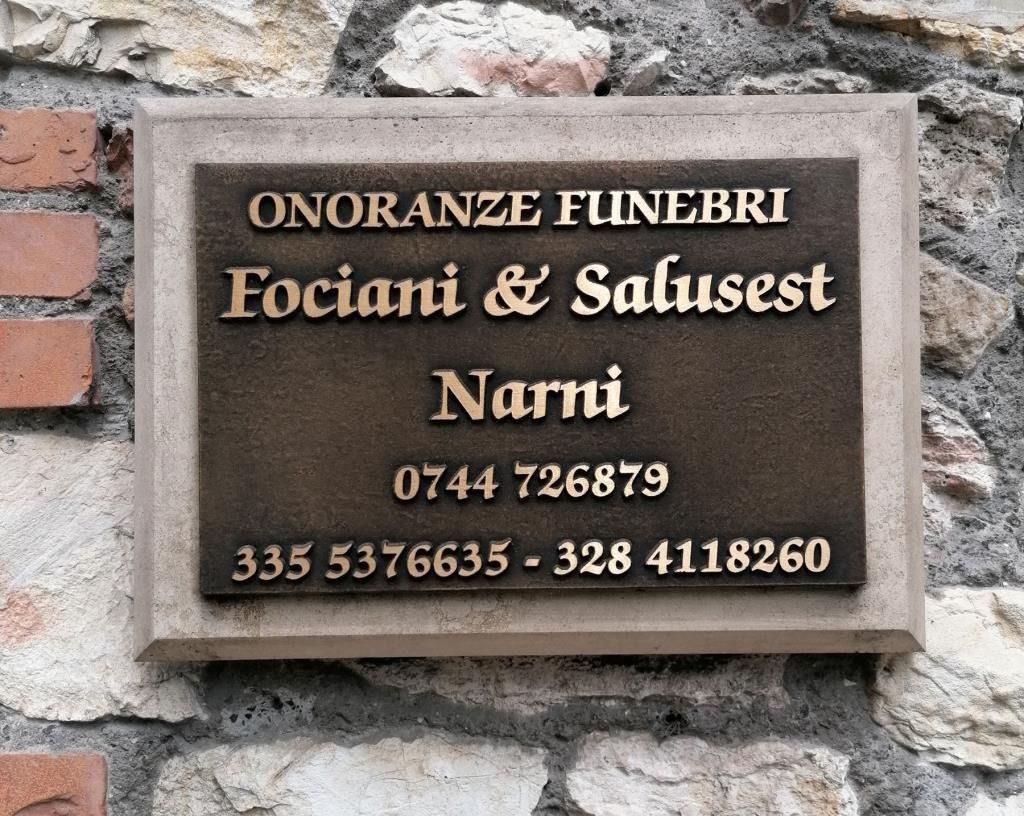 Plaque on stone wall reading “Onoranze Funebri Fociani & Salusest Nanni” with phone numbers.