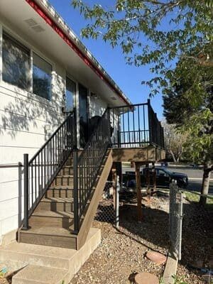 Exterior stairs with black railings leading up to a wooden deck on the side of a white house.
