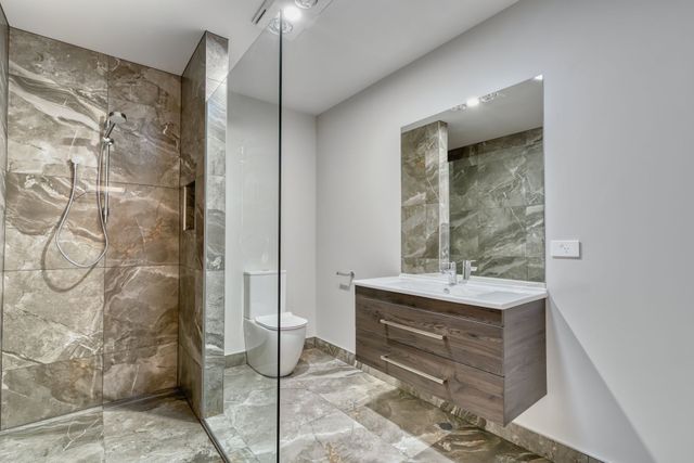 Modern bathroom with stone shower, glass partition, floating vanity, and large mirror.