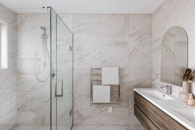 Modern white marble bathroom with glass shower, towel rack, sink, and mirror vanity